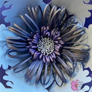 May include: A blue paper flower with a layered center, surrounded by blue paper snowflakes. The flower is made of strips of paper that are curled and layered to create a 3D effect. The snowflakes are cut out of paper and have a delicate, intricate design. The image is titled "Photo Fab Paper Flowers".