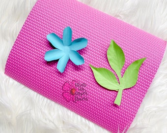 May include: A pink yoga mat with a light blue paper flower and a green paper leaf on top. The text "What to do with paper flowers" is printed on the mat.