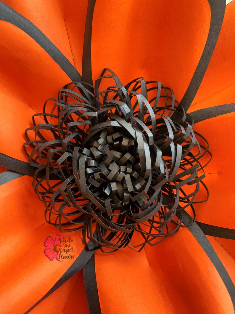May include: A large, orange paper flower with black paper petals. The center of the flower is a black paper rosette.