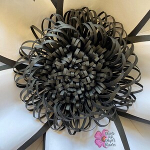 May include: Black paper flower with a layered, ruffled design. The flower is centered in a white background with black bat silhouettes and a small pink flower with the text "Photo fab paper flowers".