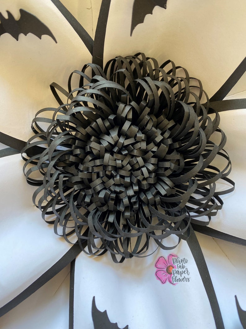 May include: Black paper flower with a layered, ruffled design. The flower is centered in a white background with black bat silhouettes and a small pink flower with the text "Photo fab paper flowers".