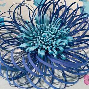 May include: A blue and turquoise paper flower with a layered design. The flower is made of multiple strips of paper that are curled and layered to create a 3D effect.