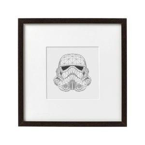 May include: Framed print featuring a geometric illustration of a Stormtrooper helmet. The artwork is rendered in black lines against a light gray background, set within a white mat and a dark brown wooden frame. A minimalist, modern design.