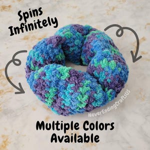 May include: A crocheted ring in shades of blue, green, and purple. The ring is designed to spin infinitely. The text "Spins Infinitely" and "Multiple Colors Available" is visible in the image.