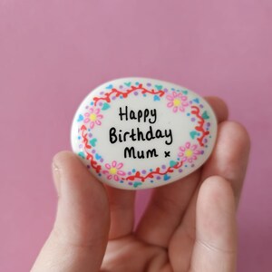 A floral wreath painted on a white pebble that can be personalised with wording in the middle.