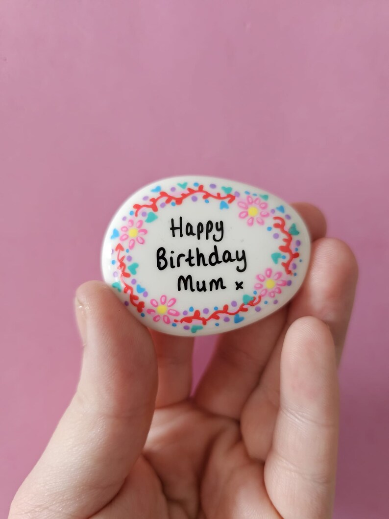 A floral wreath painted on a white pebble that can be personalised with wording in the middle.