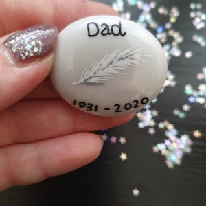 May include: White ceramic memorial stone with a feather design and the words "Dad 1931-2020"