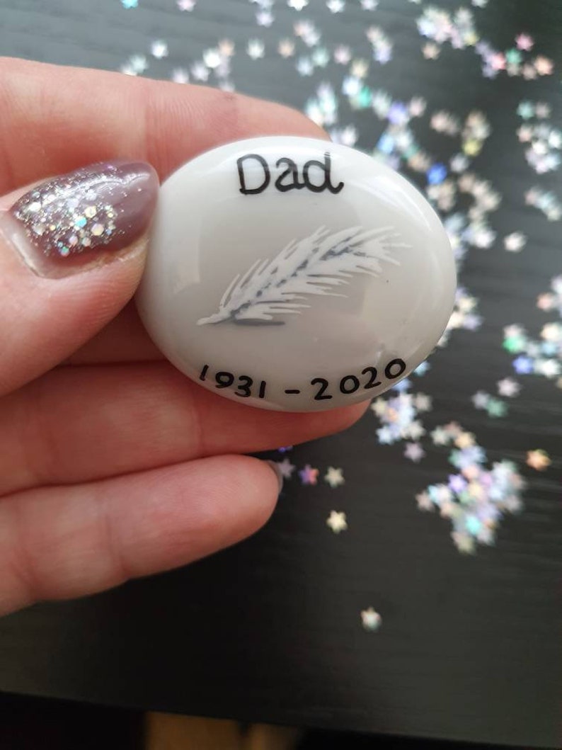 May include: White ceramic memorial stone with a feather design and the words "Dad 1931-2020"