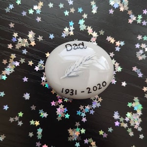May include: White ceramic memorial stone with a feather design and the text "Dad 1931-2020".