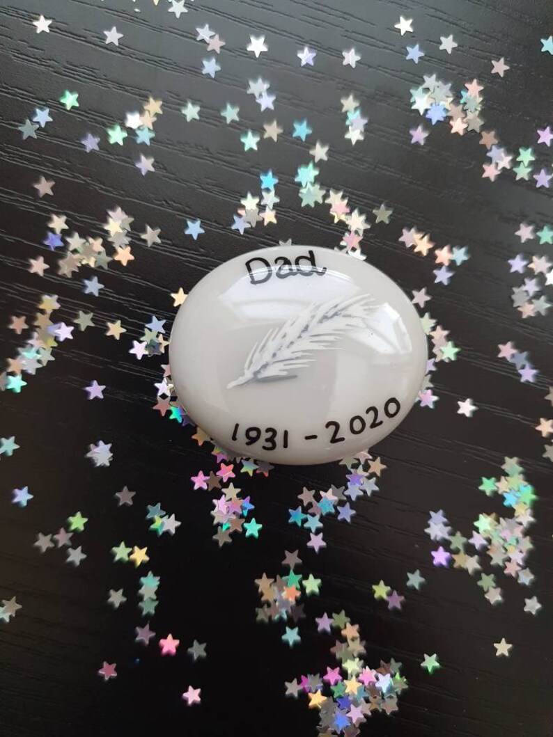 May include: White ceramic memorial stone with a feather design and the text "Dad 1931-2020".