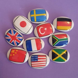 May include: A set of ten oval-shaped ceramic tiles with flags of different countries painted on them. The flags include Japan, Sweden, Germany, Turkey, South Africa, France, China, the United States, Jamaica, and the United Kingdom.