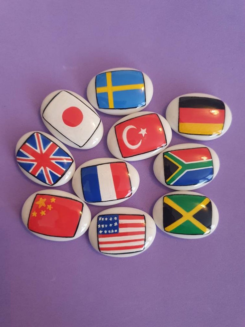 May include: A set of ten oval-shaped ceramic tiles with flags of different countries painted on them. The flags include Japan, Sweden, Germany, Turkey, South Africa, France, China, the United States, Jamaica, and the United Kingdom.