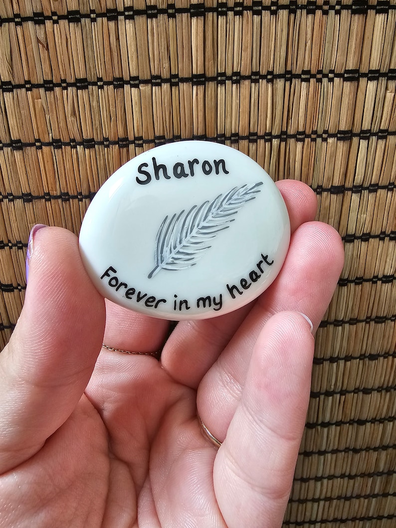 May include: White ceramic stone with a black feather design and the text "Sharon forever in my heart".