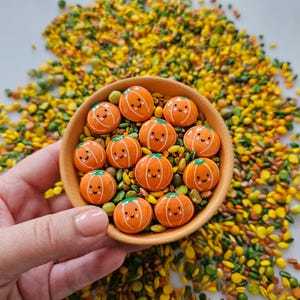 May include: A bowl filled with small orange pumpkins with happy faces, surrounded by yellow and green sprinkles.