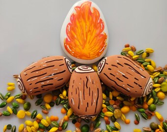 May include: A collection of hand-painted ceramic pieces. The set includes four brown log-shaped pieces with white and brown details, and one white oval piece with an orange and yellow flame design. The pieces are surrounded by colorful seeds.