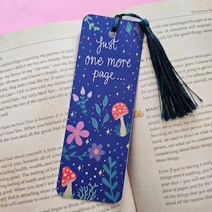 May include: A blue bookmark with a floral design and the text "Just one more page..." in white. The bookmark features a whimsical design with mushrooms, flowers, and leaves.