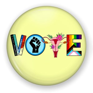 May include: A yellow button with the word "VOTE" spelled out in different symbols. The "V" is a stack of books, the "O" is a fist in a blue circle, the "T" is a pink uterus with flowers, and the "E" is a rainbow pride flag.