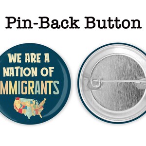 K&ouml;nnte beinhalten: Ein runder Ansteckbutton mit dem Text "WE ARE A NATION OF IMMIGRANTS" in wei&szlig;er und beiger Schrift und einer Karte der Vereinigten Staaten. Der Button ist dunkelblau und hat eine silberne Metallr&uuml;ckseite.