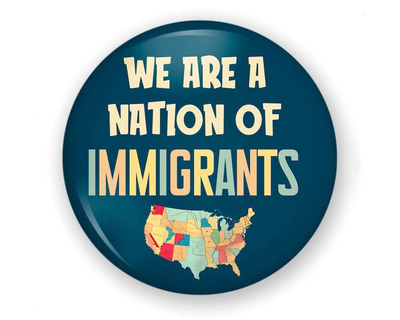 K&ouml;nnte beinhalten: Ein runder, dunkelblauer Button mit dem Text "WE ARE A NATION OF IMMIGRANTS" in einer stilisierten Schriftart. Unten befindet sich eine farbenfrohe Karte der Vereinigten Staaten. Der Button hat ein gl&auml;nzendes Finish.