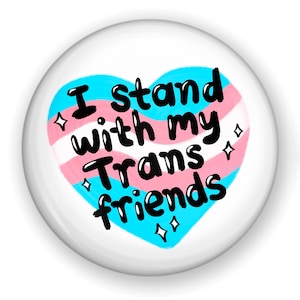 May include: A white button with a blue, pink, and white heart design. The heart has the text "I stand with my Trans friends" in black.