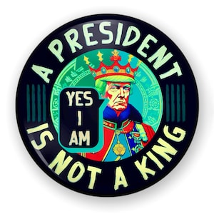 May include: A black and green button with the text "A President Is Not A King" in white. The button features a cartoon image of a person wearing a crown and a red and gold robe. The text "Yes I Am" is in a speech bubble.