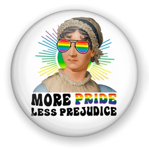 May include: A white button with a colorful rainbow design. The button features a portrait of a woman wearing rainbow sunglasses and the text "More Pride Less Prejudice".