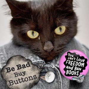 Puede incluir: Un gato negro con una chaqueta vaquera con dos botones. El gato tiene ojos amarillos y lleva dos botones. Un bot&oacute;n dice "Be Bad Buy Buttons" y el otro dice "You can't love freedom and ban books."
