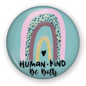 May include: A round pinback button with a teal background featuring a multi-colored rainbow graphic. The rainbow includes bands of pink, black-spotted teal, mauve, and yellow with a small black heart. The text reads HUMAN KIND Be Both.