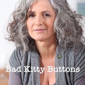 K&ouml;nnte beinhalten: Eine Frau mit grauem Haar tr&auml;gt einen grauen Strickcardigan mit einem Knopf, auf dem "Ich lese verbotene B&uuml;cher" steht. Der Text "Bad Kitty Buttons" ist &uuml;ber das Bild gelegt.