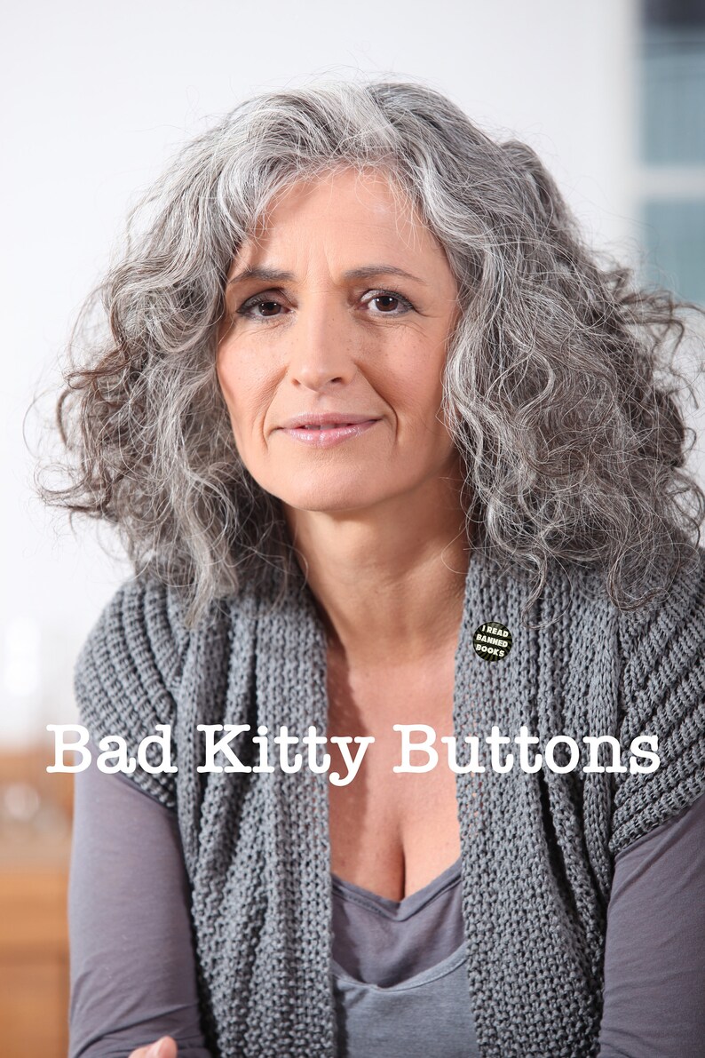 K&ouml;nnte beinhalten: Eine Frau mit grauem Haar tr&auml;gt einen grauen Strickcardigan mit einem Knopf, auf dem "Ich lese verbotene B&uuml;cher" steht. Der Text "Bad Kitty Buttons" ist &uuml;ber das Bild gelegt.
