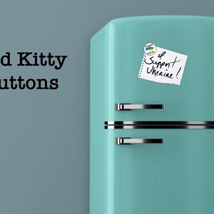 May include: A teal blue vintage refrigerator with a white note that says "I Support Ukraine!" and a small blue and yellow button with the Ukrainian flag on it.