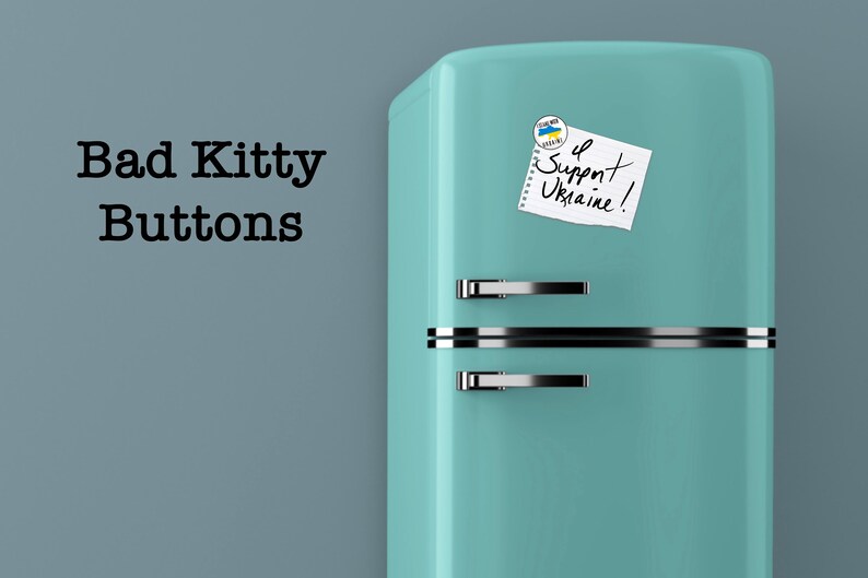 May include: A teal blue vintage refrigerator with a white note that says "I Support Ukraine!" and a small blue and yellow button with the Ukrainian flag on it.