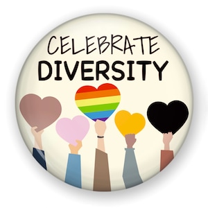 May include: A round button with the words "CELEBRATE DIVERSITY" in black. Below the text, hands hold up heart shapes in various colors, including brown, rainbow, pink, yellow, and black. The background is a light beige.