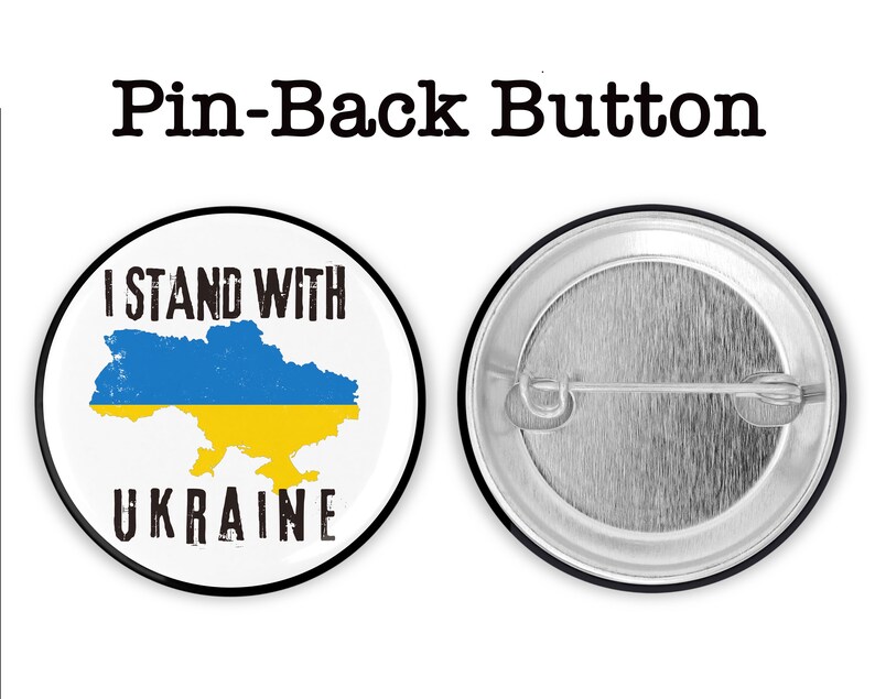 May include: A white button with a black border and the text "I Stand With Ukraine" in black. The button features a blue and yellow outline of the country of Ukraine. The back of the button is silver with a pin.