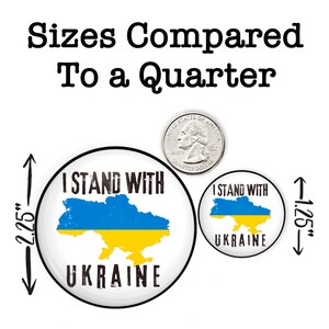 May include: Two round buttons with the text "I Stand With Ukraine" and a blue and yellow outline of the country of Ukraine. The larger button is 2.25 inches in diameter and the smaller button is 1.25 inches in diameter. A US quarter is shown for size comparison.