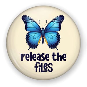 May include: A round, cream-colored button with a blue butterfly illustration. The butterfly has detailed wings with shades of blue and black. Below the butterfly, the text reads "release the files" in a dark blue font.