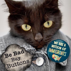 K&ouml;nnte beinhalten: Eine schwarze Katze tr&auml;gt eine Jeansjacke mit zwei Kn&ouml;pfen. Die Katze hat gelbe Augen. Ein Knopf sagt "Be Bad Buy Buttons" und der andere sagt "We Are A Nation of Immigrants" mit einer Karte der USA.
