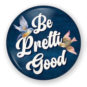 May include: A round, navy blue button with the words "Be Pretti Good" in white script. Two watercolor birds, one blue and orange, the other brown and pink, are featured on the button.