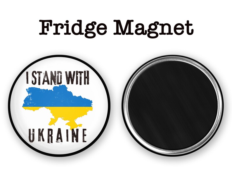 May include: A round fridge magnet with a white background and a blue and yellow outline of Ukraine. The text "I Stand With Ukraine" is printed in black above the outline and "UKRAINE" is printed in black below the outline.