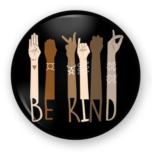 May include: A black button with a design of six hands in different skin tones, each making a different hand gesture. The hands are surrounded by the text "BE KIND".