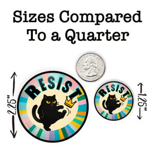 May include: Two round buttons with a black cat graphic and the word "RESIST". The larger button is 2.25 inches in diameter, and the smaller is 1.25 inches. The buttons have a colorful striped background and a gold crown.