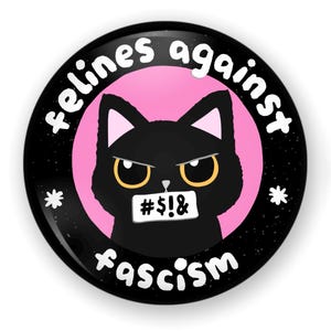 May include: A black and white button with a black cat wearing a tape over its mouth with the text "#S!&" on it. The cat is in front of a pink circle with the text "felines against fascism" around it.