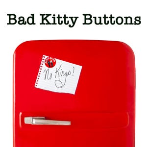 May include: A bright red refrigerator with a silver handle and the text "Bad Kitty Buttons" at the top. A small piece of paper with the words "No Kings!" is attached to the door.