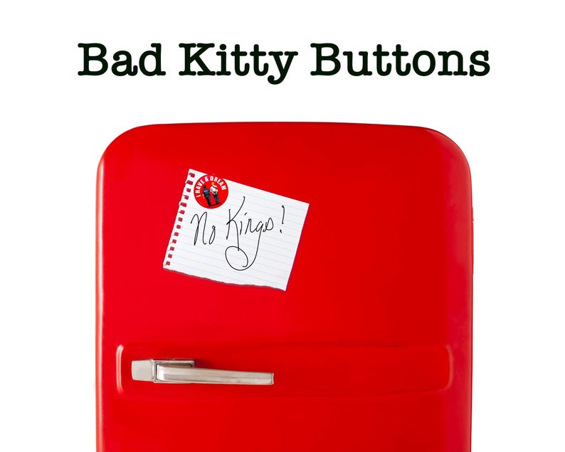 May include: A bright red refrigerator with a silver handle and the text "Bad Kitty Buttons" at the top. A small piece of paper with the words "No Kings!" is attached to the door.