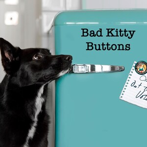 Może przedstawiać: Czarno-biały pies patrzy w g&oacute;rę na turkusową lod&oacute;wkę. Pies trzyma w pysku klamkę drzwi. Tekst na lod&oacute;wce brzmi "Bad Kitty Buttons". Notatka na drzwiach m&oacute;wi "Let's get out the Vote!"