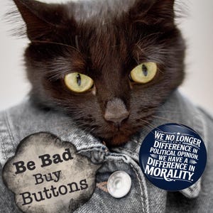 May include: A black cat wearing a denim jacket with two buttons. The cat has yellow eyes and is wearing two buttons. One button says "Be Bad Buy Buttons" and the other says "We no longer difference in political opinion. We have a difference in morality."