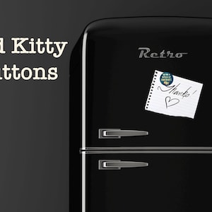 K&ouml;nnte beinhalten: Ein schwarzer Retro-K&uuml;hlschrank mit silbernen Griffen und dem Wort "Retro" in silbernen Buchstaben. Ein Notizblock mit dem Wort "Danke!" und einem Herz ist an der T&uuml;r befestigt. Die Worte "Bad Kitty Buttons" sind in wei&szlig;em Text.