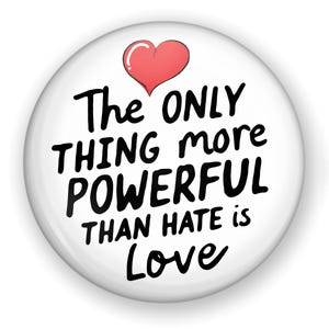May include: A white button with the text "The ONLY thing more POWERFUL than HATE is Love" in black, with a red heart at the top. The button has a glossy finish and a slight shadow.