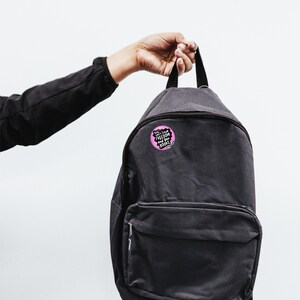 Puede incluir: Una mochila negra con un bot&oacute;n redondo prendido. El bot&oacute;n es rosa con texto blanco que dice "You can't Love Freedom and Ban Books". Las palabras "BAD Kitty BUTTONS" est&aacute;n encima de la mochila.