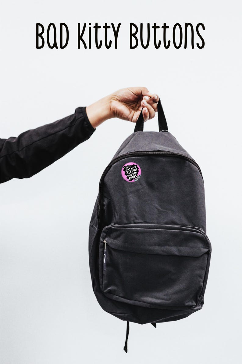 Puede incluir: Una mochila negra con un bot&oacute;n redondo prendido. El bot&oacute;n es rosa con texto blanco que dice "You can't Love Freedom and Ban Books". Las palabras "BAD Kitty BUTTONS" est&aacute;n encima de la mochila.